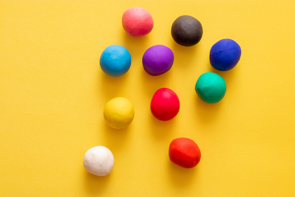 Multiple colored plasticine balls on a yellow background. All scatered randomly, children's toys and games